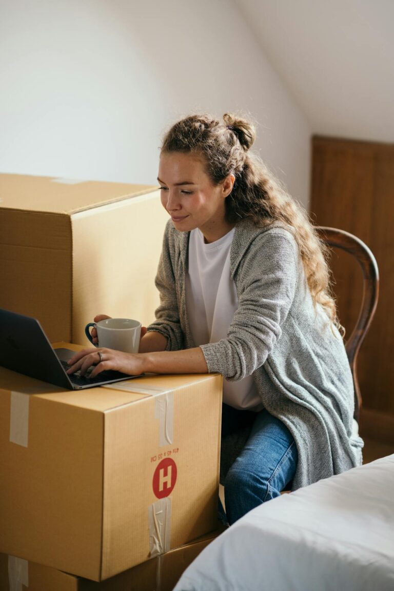 Relaxed woman using laptop in room with carton boxes